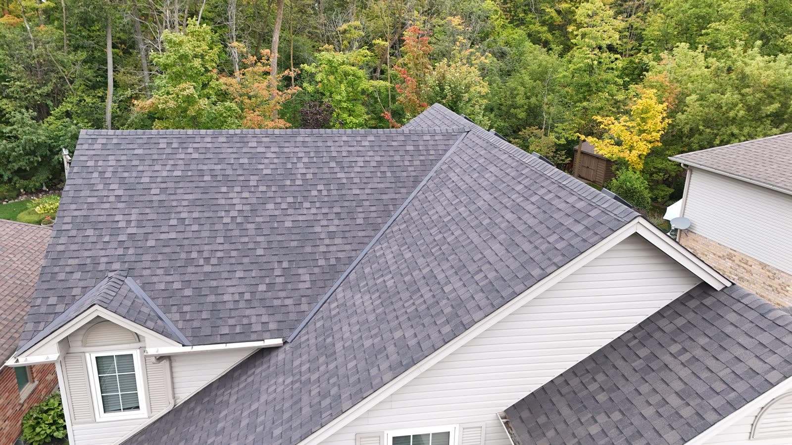 A finished Max Def Espresso shingle roof with a small gable dormer, backing onto woodland, photographed by drone from just above the ridge