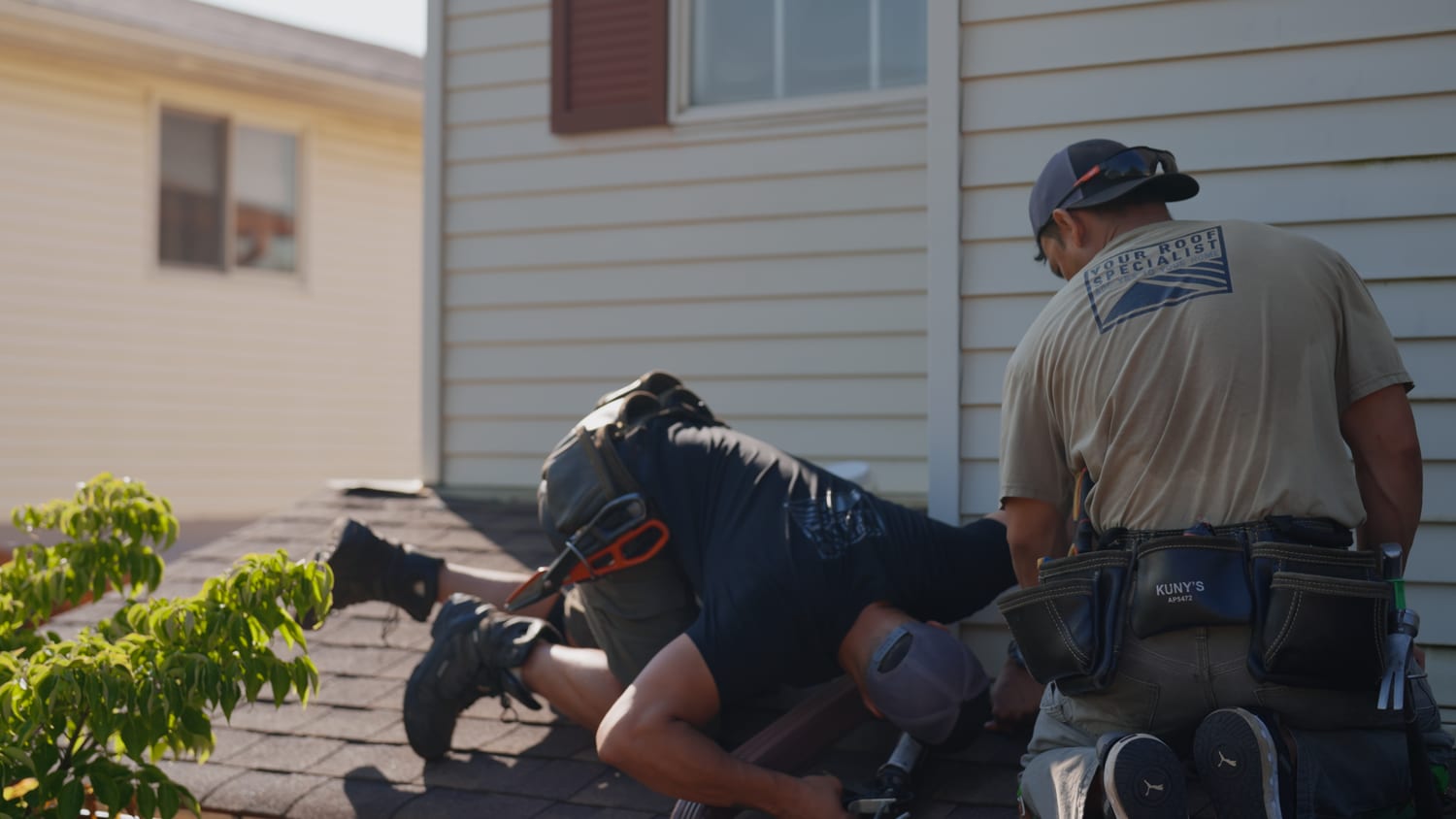 Two Your Roof Specialist crew members working on a roof-to-wall junction where the roofline meets siding