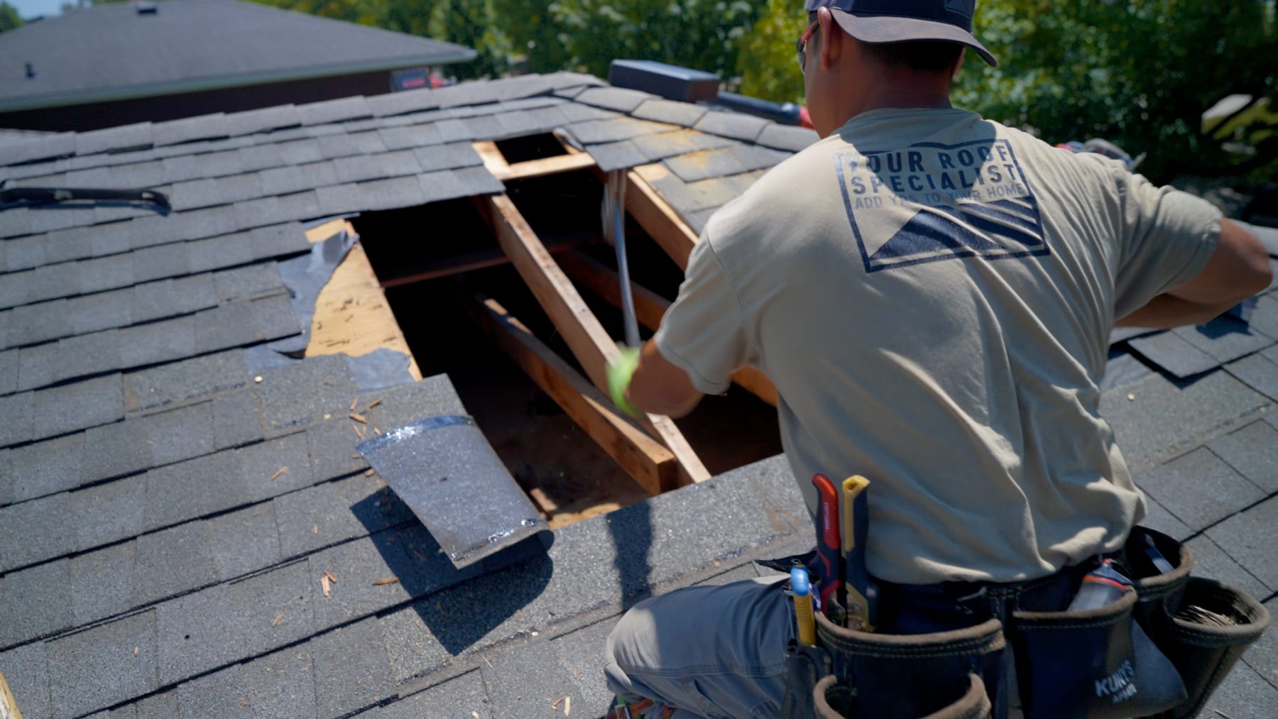 Your Roof Specialist crew member on a roof with a section of rotted decking removed, exposing the rafters and framing below