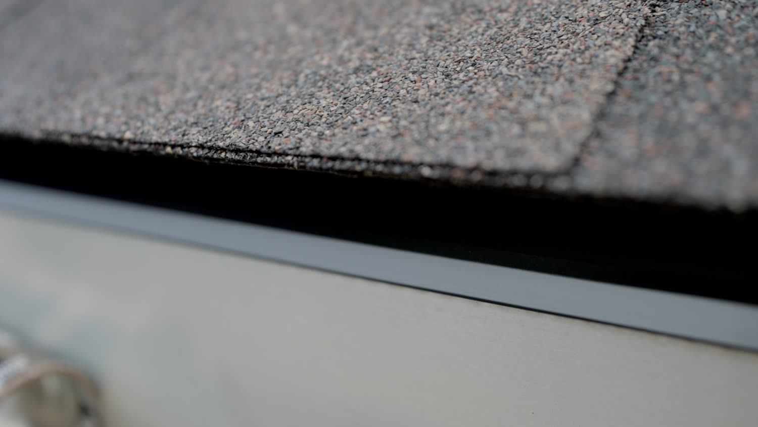 Close view of the eave on a finished roof, the shingle overhanging new drip edge metal above the fascia