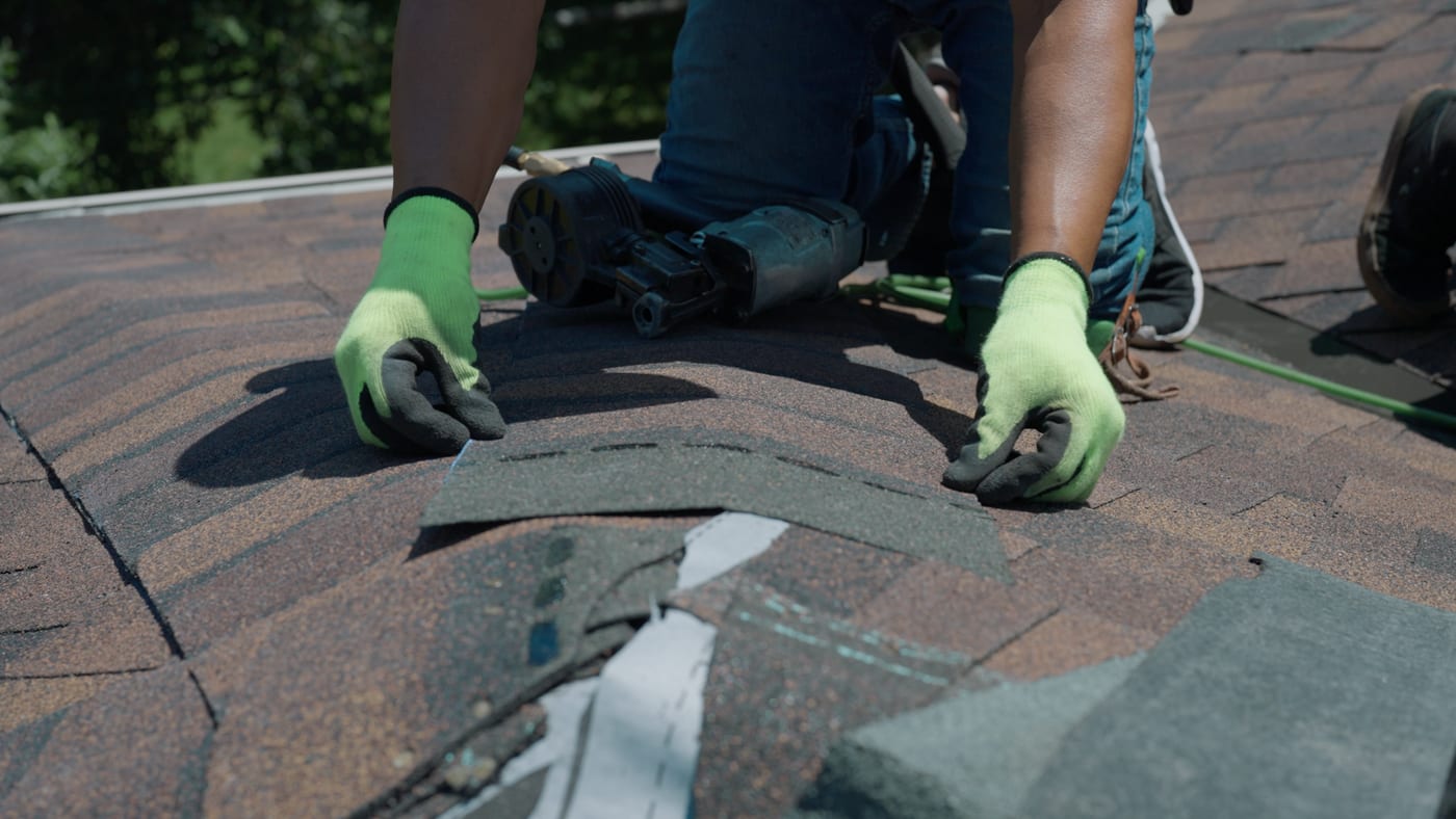Hands setting and sealing replacement shingles over new underlayment during a targeted roof repair