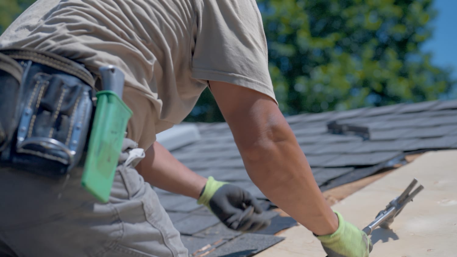 Crew member carefully lifting shingles with a flat bar to inspect the decking underneath during a roof repair
